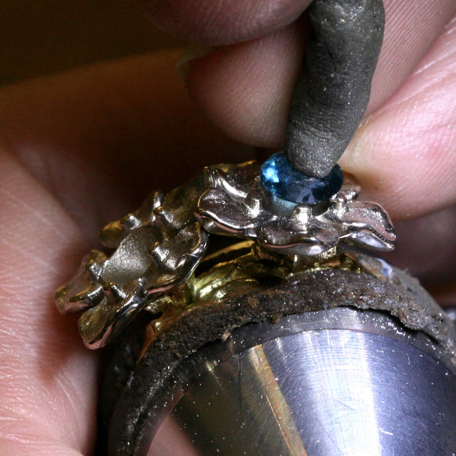 A making of image of a double flower ring getting a stone set on it.